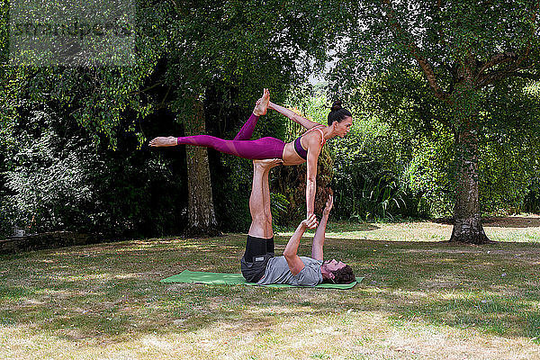 Junger Mann praktiziert Yoga im Garten  auf dem Rücken liegend balanciert Frau auf Füßen