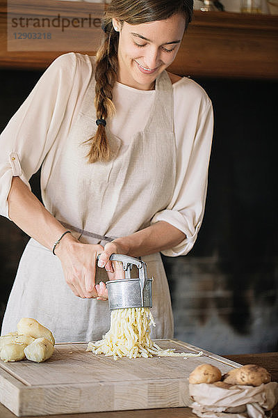 Frau benutzt Kartoffelpresse zur Zubereitung von Gnocchi