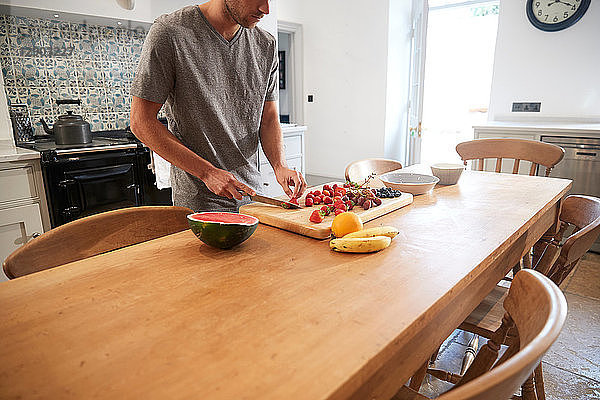 Junger Mann schneidet frisches Obst am Küchentisch