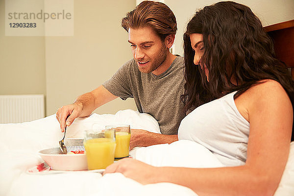 Ehepaar beim Frühstück mit Obst und Orangensaft im Bett