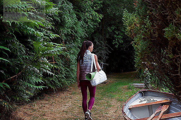 Frau mit Yogamatte beim Spaziergang durch den Garten