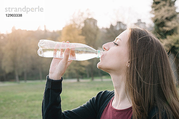 Junge Frau trinkt aus Wasserflasche im Park