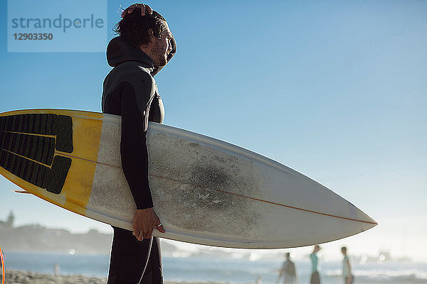 Männlicher Surfer im Nassanzug mit Surfbrett am Strand  Camps Bay Beach  Kapstadt  Südafrika