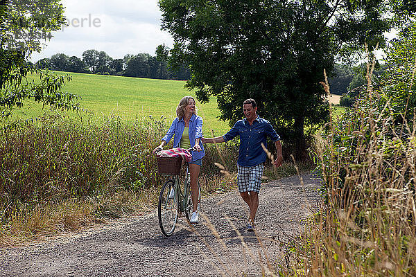 Ausgewachsenes Paar beim Spazierengehen und Radfahren auf der Landstraße