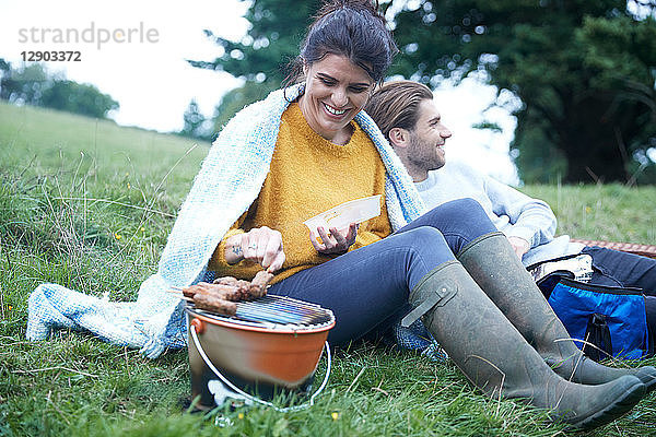 Paar sitzt im ländlichen Feld und kocht auf dem Barbecue-Grill