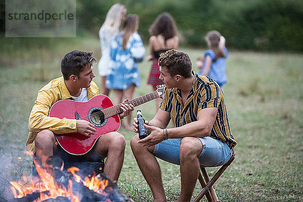 Junger Mann spielt Gitarre bei Lagerfeuer-Party im Park