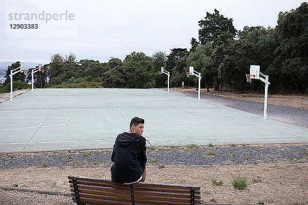 Männlicher jugendlicher Basketballspieler blickt von der Parkbank am Basketballfeld zurück