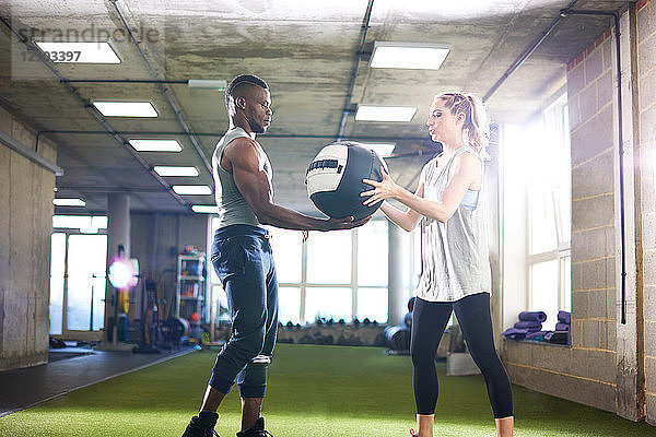 Trainer übergibt Medizinball an Klientin im Fitnessstudio
