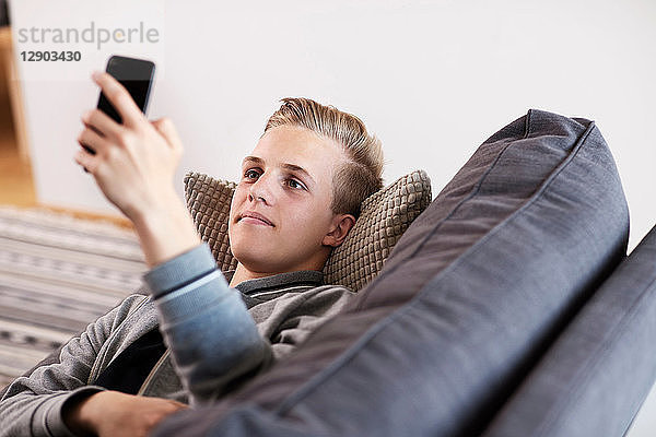 Teenager  der sich auf dem Sofa entspannt und auf ein Smartphone schaut