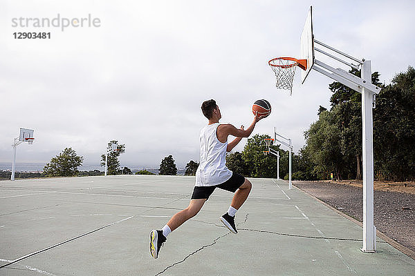 Männlicher jugendlicher Basketballspieler springt mit dem Ball in Richtung Basketballkorb