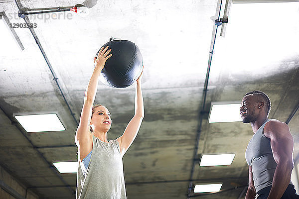 Trainer beobachtet weiblichen Klienten beim Heben eines Medizinballs im Fitnessstudio