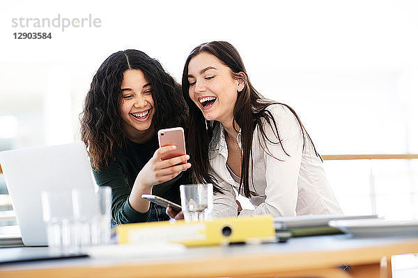 Teenager-Schülerinnen am Klassenpult lachen über Smartphone