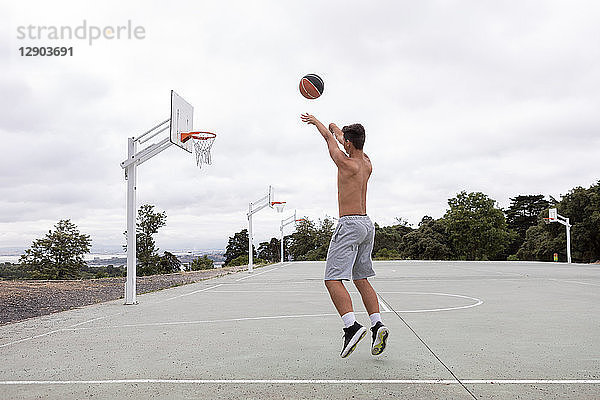 Männlicher jugendlicher Basketballspieler springt und wirft Ball in Richtung Basketballkorb