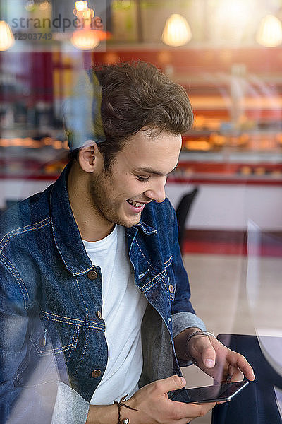 Männlicher Student schaut auf Smartphone im Cafe-Fensterplatz  Blick durch das Fenster
