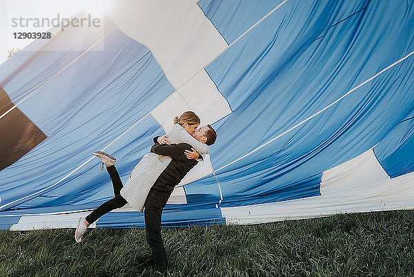 Frisch verlobtes Paar küsst sich  im Hintergrund ein Heißluftballon