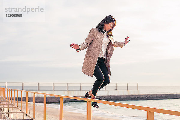 Frau springt am Strand vom Geländer