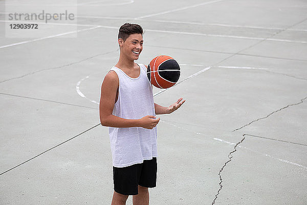 Männlicher jugendlicher Basketballspieler auf dem Basketballfeld beim Werfen und Fangen von Bällen