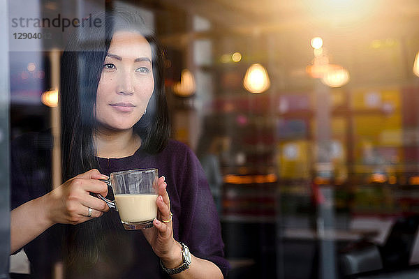 Mittelgroße erwachsene Frau mit Kaffee  die vom Fensterplatz des Cafés hinaussieht