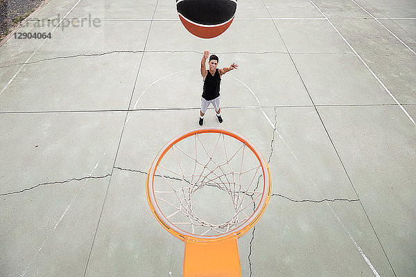 Männlicher Teenager-Basketballspieler  der den Ball in Richtung Basketballkorb wirft  Blick aus hohem Winkel