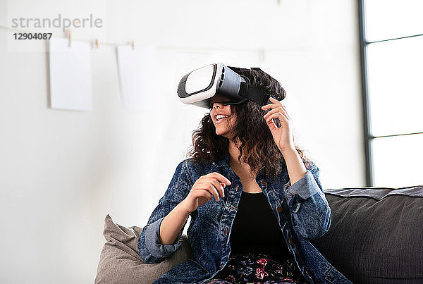 Teenager-Mädchen auf dem Sofa schaut durch ein Virtual-Reality-Headset