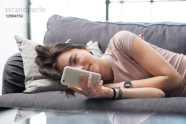 Teenager-Mädchen liegt auf Sofa und schaut auf Smartphone