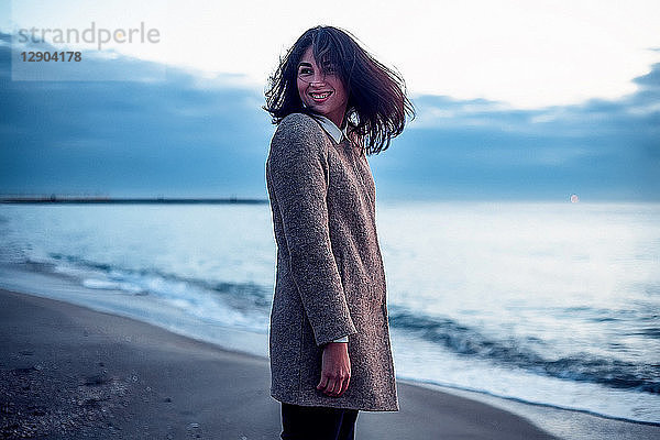 Porträt einer jungen Frau  die am Strand steht  über die Schulter schaut und lächelt