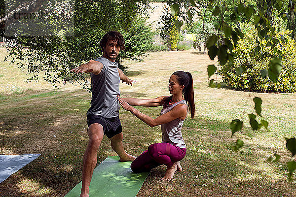 Weibliche Yogalehrerin  die einem jungen Mann Yoga im Garten beibringt  Kriegerhaltung