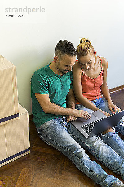 Couple sitting side by side on the floor of new home looking together at laptop