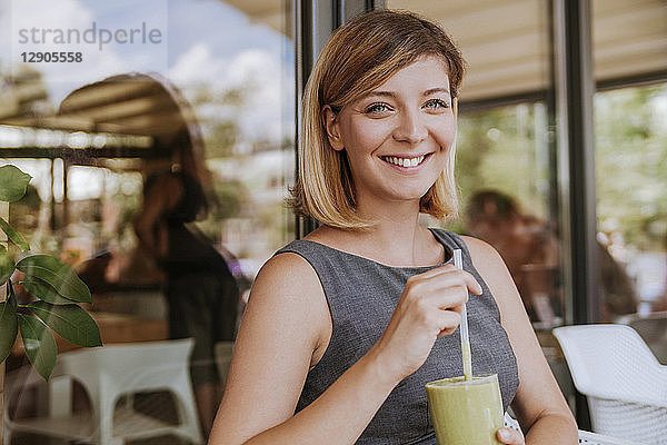 Portrait of smiling young woman with smoothie in a cafe