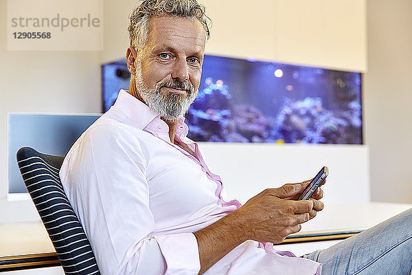 Portrait of confident businessman sitting in office using cell phone