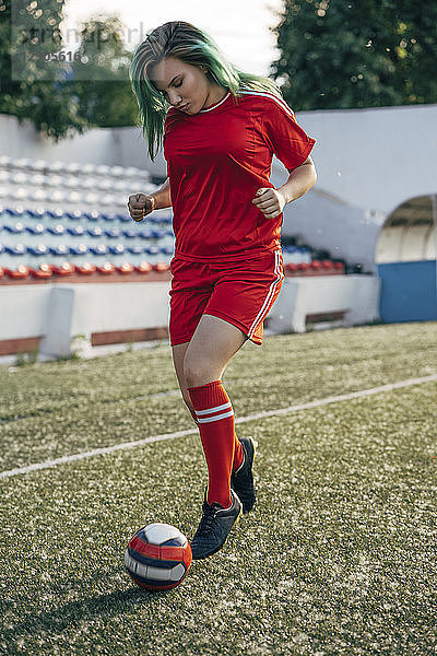 Young woman playing football on football ground dribbling with the ball