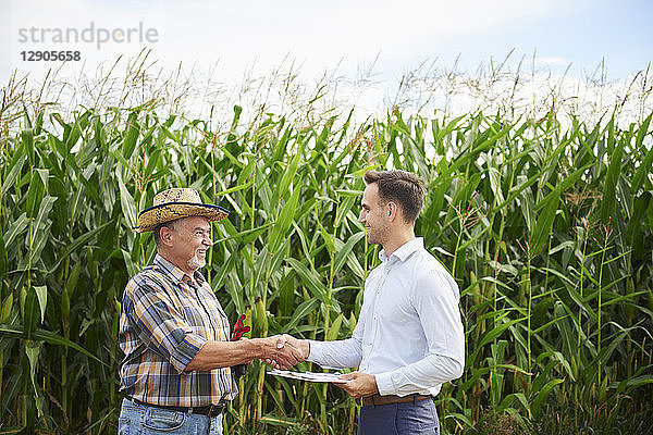 Farmer and businessman shaking hands at the cornfield