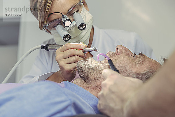 Patient getting dental treatment  dentist using dental drill and head magnifiers and light