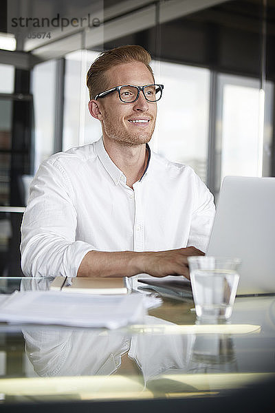 Smiling businessman with laptop on desk in office