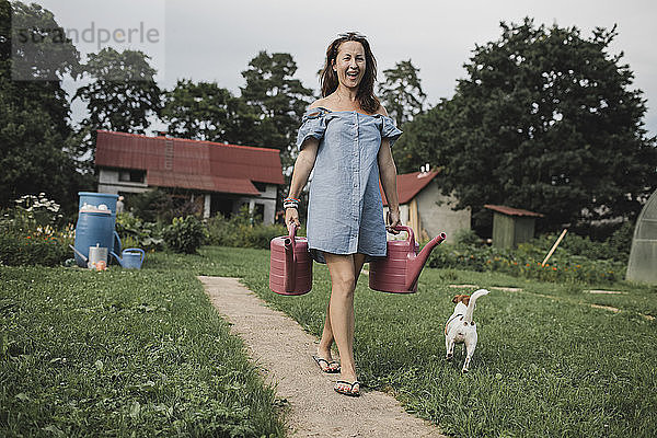 Happy woman with Jack Russel Terrier carrying watering cans in garden