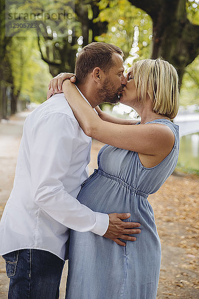 Mature pregnant couple kissing in park