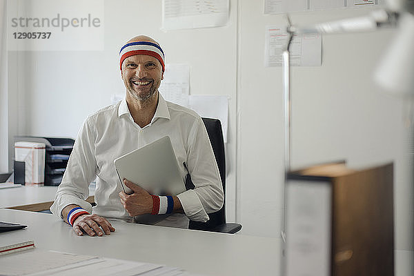 Businessman sitting in office  wearing sweat bands  holding laptop