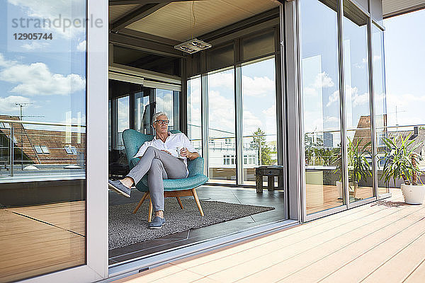 Mature man relaxing in armchair at roof terrace at home