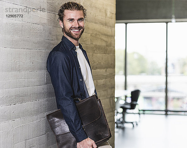 Smiling casual businessman standing on office floor holding briefcase