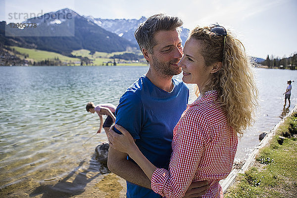 Austria  Tyrol  Walchsee  happy couple embracing at the lake with family in background