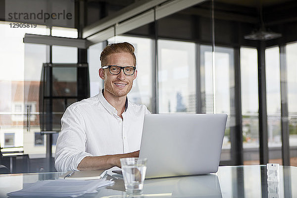 Portrait of smiling businessman using laptop on desk in office