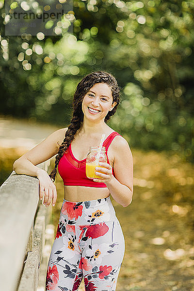 Young woman drinking juice after practicing Pilates in an urban park