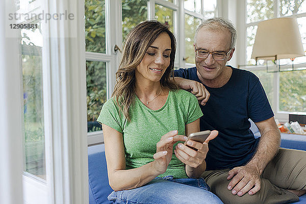 Smiling mature couple sitting on couch at home sharing cell phone