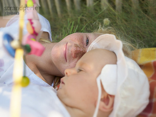 Smiling girl lying with baby girl on blanket on a meadow