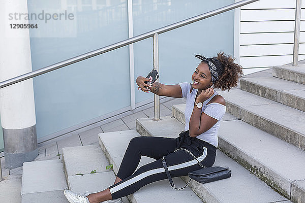 Smiling young woman sitting on stairs taking selfie with smartphone