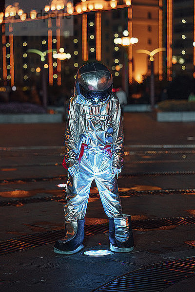Spaceman standing at a lamp on a city square at night
