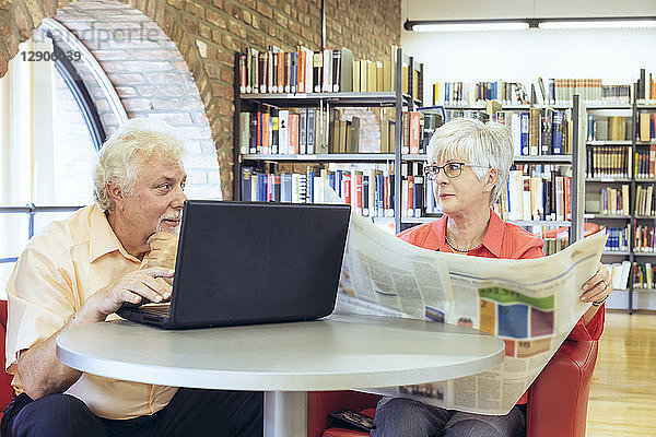 Senior couple with laptop and newspaper in a city library