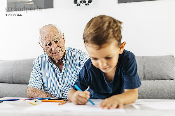Portrait of smiling grandfather watching his grandson drawing with coloured pencils