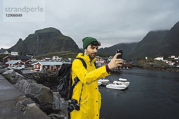 Norway  Lofoten  young man in a fishing village at the coast taking a selfie