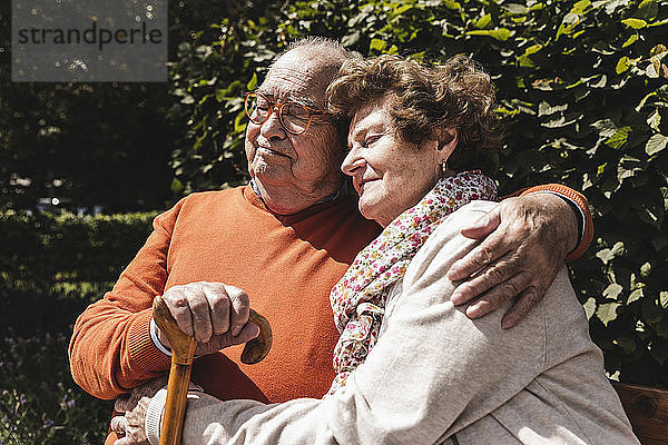 Senior couple sitting on bench in a park  with arms around